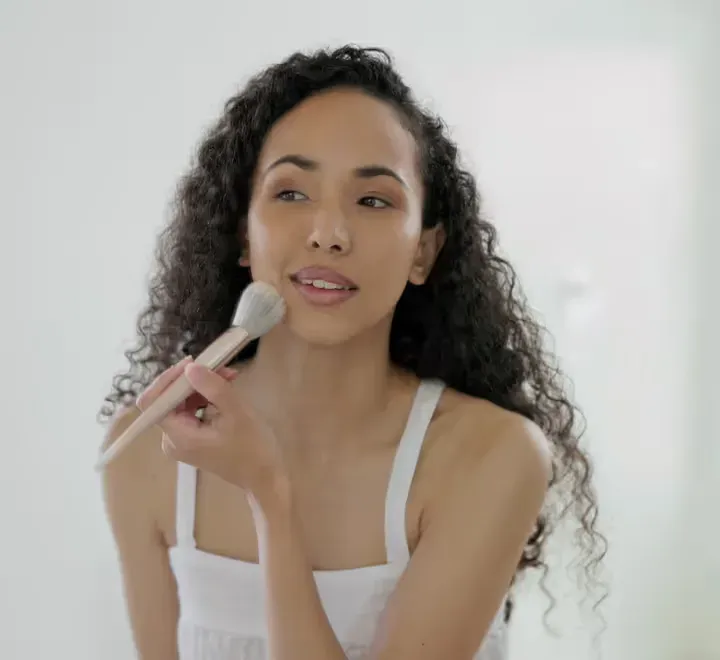 A woman with curly hair applying makeup with a brush